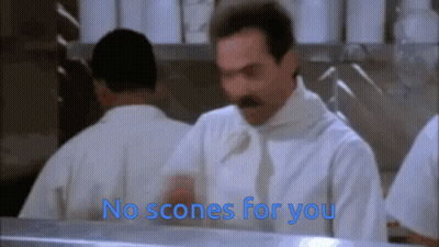 A Man With A Mustache Is Standing In Front Of A Counter With The Words " No Scones For You " Above Him GIF