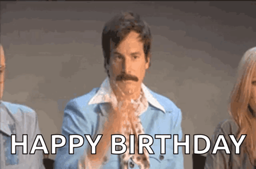 A Man With A Mustache Is Standing In Front Of A Group Of People And Says `` Happy Birthday '' . GIF