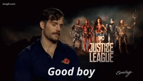 A Man With A Mustache Is Standing In Front Of A Poster For The Justice League GIF