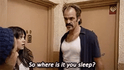A Man With A Mustache Is Standing Next To A Woman In A Room And Talking To Her . GIF