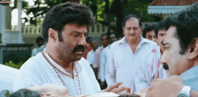 A Man With A Mustache Is Talking To Another Man In Front Of A Sign That Says " Sri Balaji Video " GIF