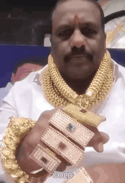 A Man With A Mustache Is Wearing A Lot Of Gold Jewelry And Holding A Bracelet . GIF