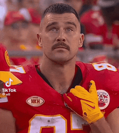A Man With A Mustache Is Wearing A Red Jersey And Yellow Gloves While Standing In Front Of A Crowd . GIF