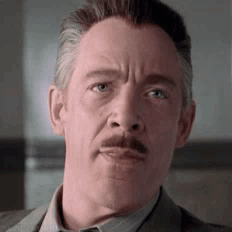 A Man With A Mustache Is Wearing A Suit And Tie And Looking At The Camera . GIF
