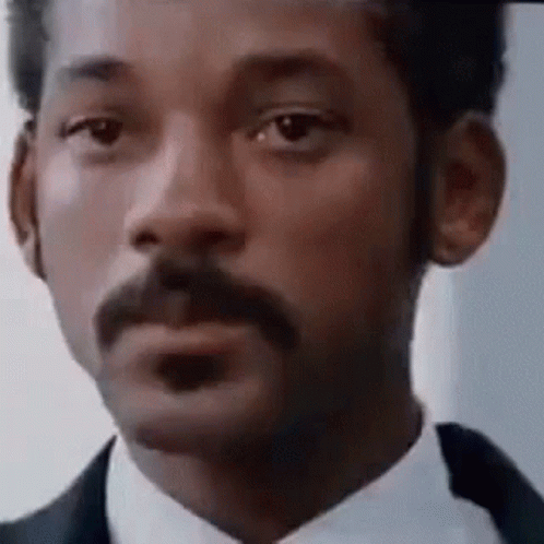 A Man With A Mustache Is Wearing A Suit And Tie And Making A Funny Face . GIF