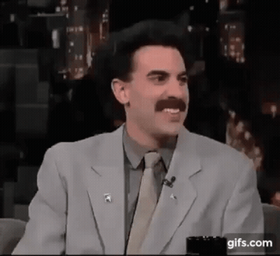 A Man With A Mustache Is Wearing A Suit And Tie And Talking On A Microphone . GIF