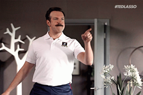 A Man With A Mustache Is Wearing A White Shirt That Says Ted Lasso On It GIF