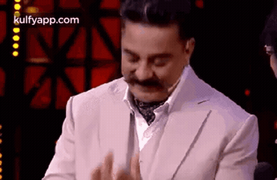 A Man With A Mustache Is Wearing A White Suit And Tie And Clapping His Hands . GIF