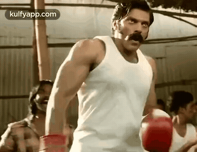 A Man With A Mustache Is Wearing Boxing Gloves And A Tank Top . GIF
