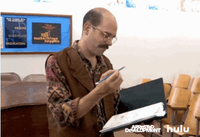 A Man With A Mustache Is Writing On A Piece Of Paper In Front Of A Sign That Says Yell Makes Dogs Happy GIF