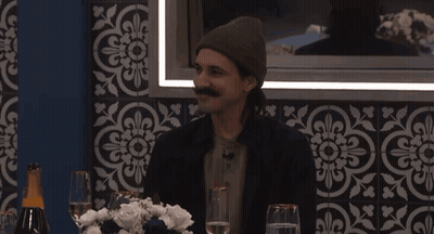 A Man With A Mustache Sits At A Table With Wine Glasses GIF
