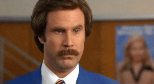A Man With A Mustache Wearing A Blue Suit And Tie Looks At The Camera GIF