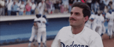 A Man With A Mustache Wearing A Dodgers Jersey Is Standing On A Baseball Field . GIF