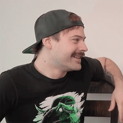 A Man With A Mustache Wearing A Hat And A Black Shirt With A Green Monster On It GIF