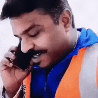 A Man With A Mustache Wearing An Orange Vest Is Talking On A Cell Phone . GIF