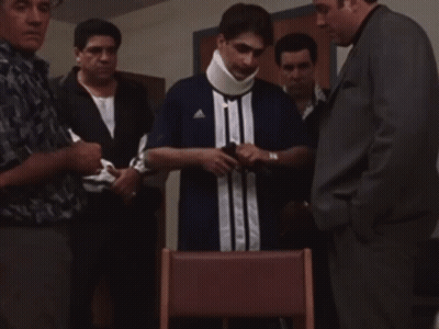 A Man With A Neck Brace Is Surrounded By Men GIF