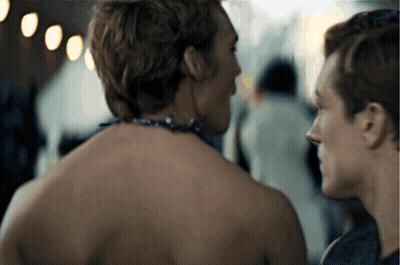 A Man With A Necklace Around His Neck Is Looking At Another Man GIF