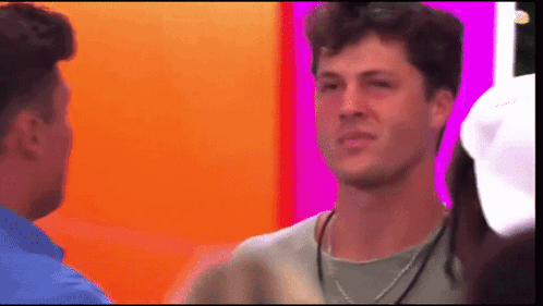 A Man With A Necklace Around His Neck Is Talking To Another Man . GIF