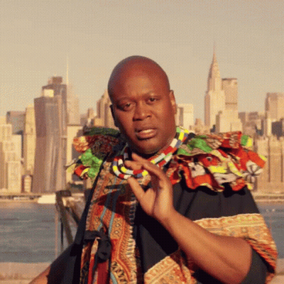 A Man With A Necklace Around His Neck Stands In Front Of A City GIF