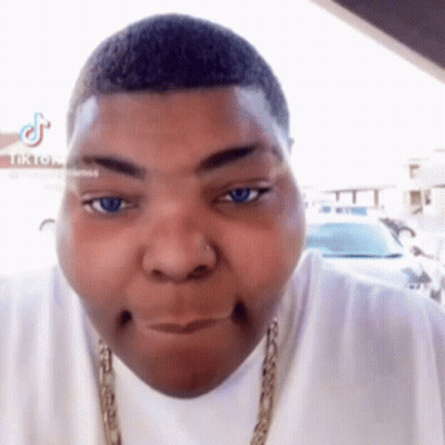 A Man With A Nose Ring Is Making A Funny Face While Wearing A White Shirt And A Gold Chain . GIF