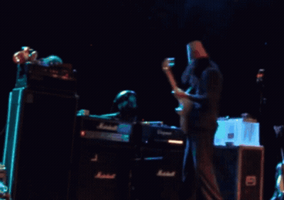 A Man With A Paper Bag On His Head Is Playing A Guitar In Front Of A Marshall Amplifier GIF