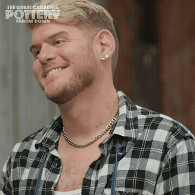 A Man With A Plaid Shirt And A Chain Around His Neck Is Smiling For The Great Canadian Pottery Show GIF