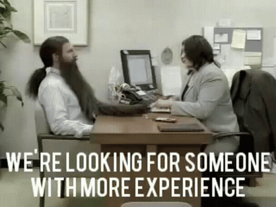 A Man With A Ponytail Is Sitting At A Desk Talking To A Woman . GIF
