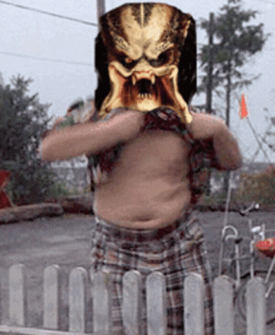 A Man With A Predator Mask On His Head Stands In Front Of A Fence GIF