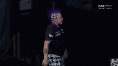A Man With A Purple Mohawk Stands In Front Of A Bbc America Logo GIF