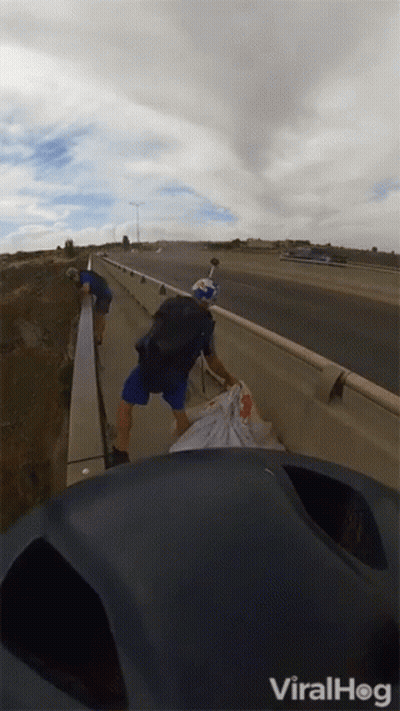 A Man With A Red Bull Helmet Is Walking Across A Highway GIF