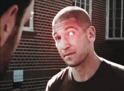 A Man With A Red Eye Is Talking To Another Man In Front Of A Brick Building GIF