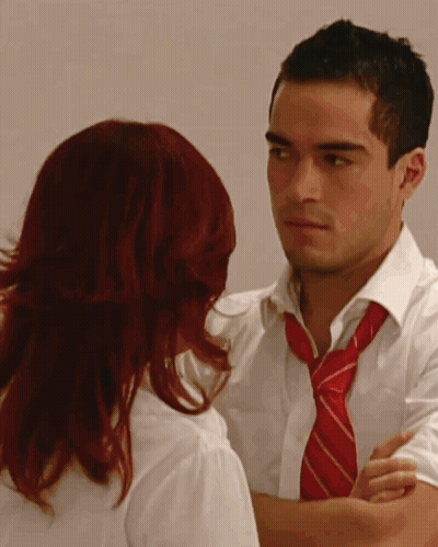 A Man With A Red Tie And A Woman With Red Hair Are Looking At Each Other GIF