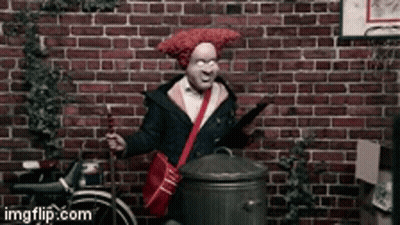 A Man With A Red Wig Is Standing In Front Of A Brick Wall Holding A Trash Can GIF