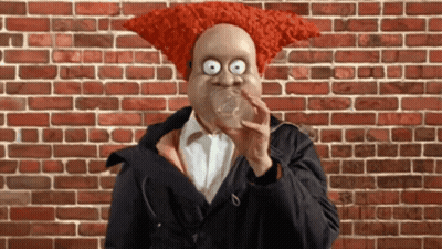 A Man With A Red Wig On His Head Blowing A Bubble GIF