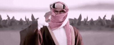 A Man With A Scarf Around His Face Is Standing In Front Of A Field . GIF