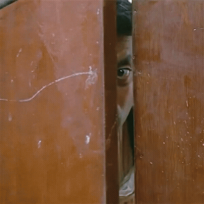 A Man With A Scarf Around His Neck Is Peeking Out Of A Doorway GIF