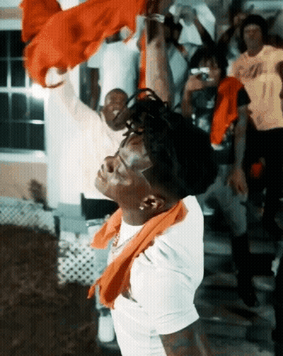 A Man With A Scarf Around His Neck Is Standing In Front Of A Crowd GIF