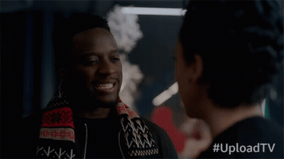 A Man With A Scarf Around His Neck Smiles While Talking To A Woman With #Uploadtv Written Below Him GIF