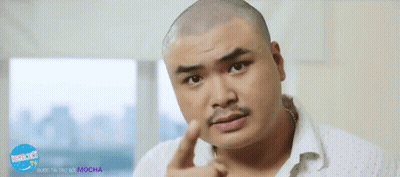 A Man With A Shaved Head And A Moustache Is Pointing At Something In Front Of A Sign That Says Mocha Tv GIF