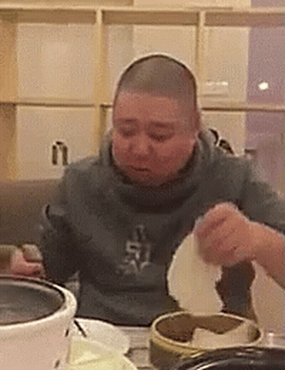 A Man With A Shaved Head Is Sitting At A Table Eating Food From A Bowl . GIF
