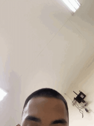 A Man With A Shaved Head Looks At The Camera With A Chair In The Background GIF