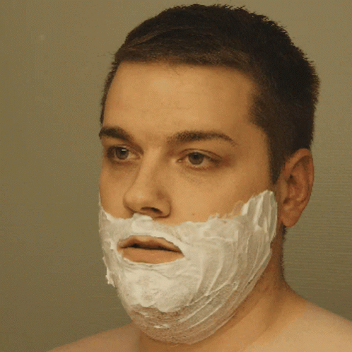 A Man With A Shaving Cream On His Face Looks At The Camera GIF