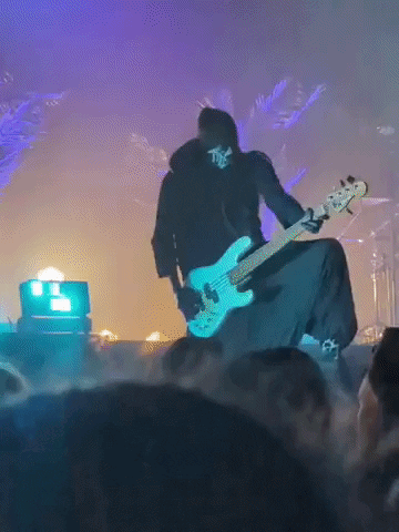 A Man With A Skull On His Face Is Playing A Guitar On Stage GIF