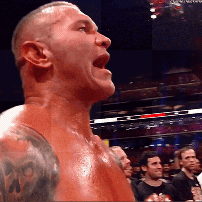 A Man With A Skull Tattoo On His Arm Stands In Front Of A Crowd With His Mouth Open GIF