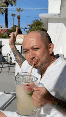 A Man With A Straw In His Mouth Drinking A Drink From A Pitcher GIF