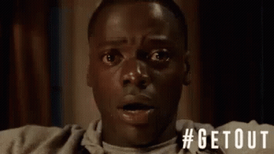 A Man With A Surprised Look On His Face Is Sitting On A Couch In A Room . GIF