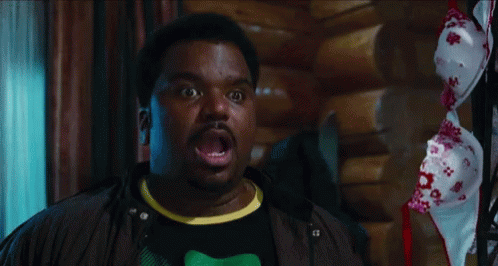 A Man With A Surprised Look On His Face Stands In Front Of A Bra Hanging On A Rack GIF
