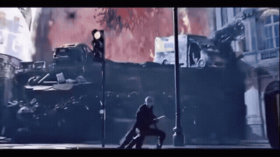 A Man With A Sword Is Walking Down A Street In Front Of A Fire . GIF