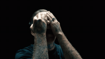 A Man With A Tattoo On His Arm Covering His Face GIF