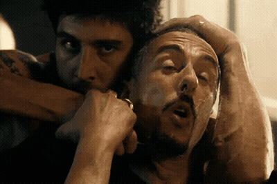 A Man With A Tattoo On His Arm Holds Another Man 'S Head In His Hands GIF